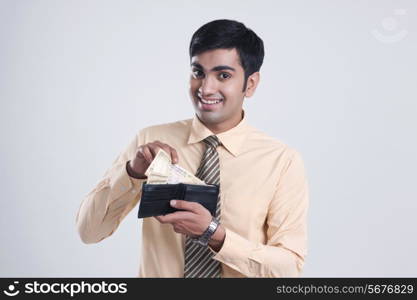 Portrait of smiling businessman showing money in wallet over gray background