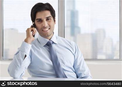 Portrait of smiling businessman speaking on phone call at office