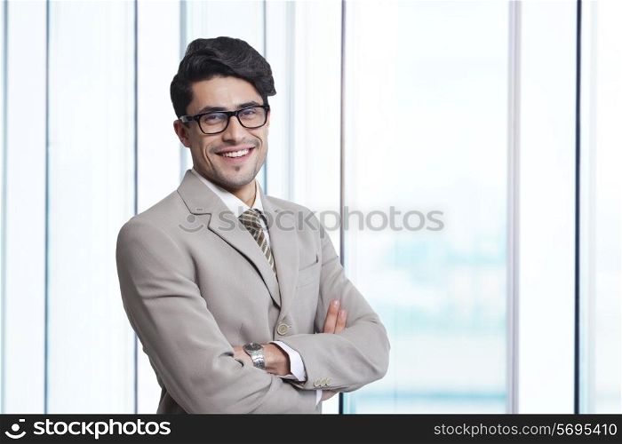 Portrait of smiling businessman standing arms crossed in office