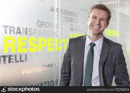 Portrait of smiling businessman standing by text on glass wall at modern office