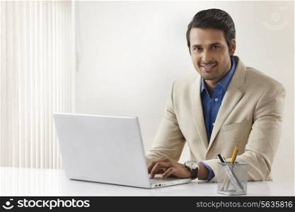 Portrait of smiling businessman using laptop at office desk
