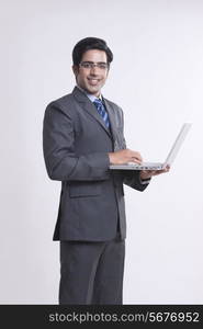 Portrait of smiling businessman using laptop over gray background