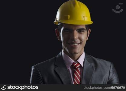 Portrait of smiling businessman wearing hardhat against black background