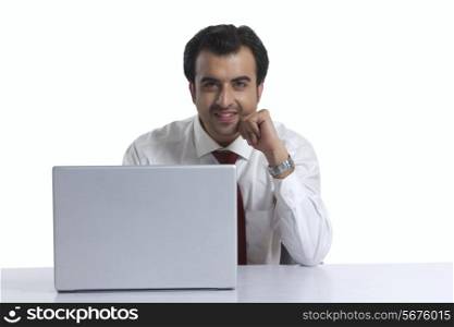 Portrait of smiling businessman with laptop at desk against white background