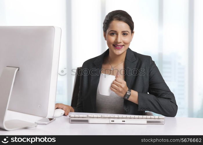 Portrait of smiling businesswoman having coffee at desk in office