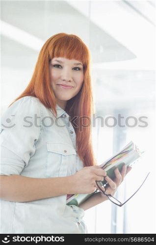 Portrait of smiling businesswoman holding files in creative office
