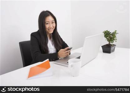 Portrait of smiling businesswoman using cell phone at office desk