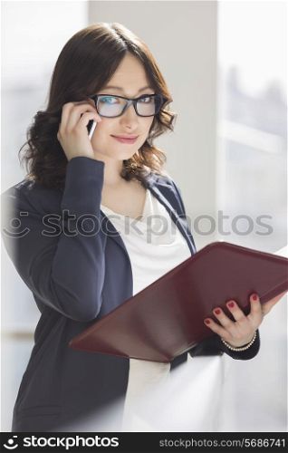 Portrait of smiling businesswoman using cell phone while holding file in office