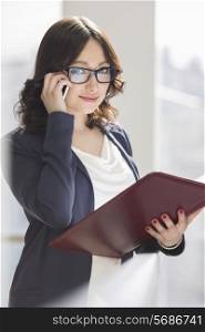 Portrait of smiling businesswoman using cell phone while holding file in office