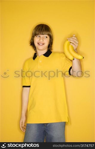 Portrait of smiling Caucasian boy holding bunch of bananas standing against yellow background.