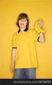 Portrait of smiling Caucasian boy holding bunch of bananas standing against yellow background.