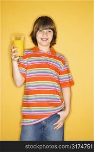 Portrait of smiling Caucasian boy holding glass of orange juice and standing against yellow background.