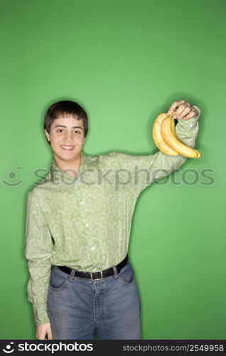 Portrait of smiling Caucasian teen boy holding bananas in air standing against green background.
