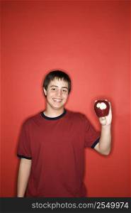 Portrait of smiling Caucasian teen boy holding partially eaten apple against red background.