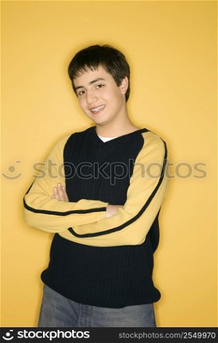 Portrait of smiling Caucasian teen boy with crossed arms standing against yellow background.