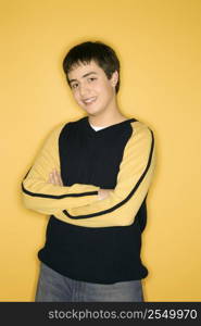 Portrait of smiling Caucasian teen boy with crossed arms standing against yellow background.