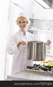 Portrait of smiling chef holding steel pot over stove in kitchen at restaurant