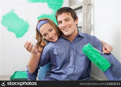 Portrait of smiling couple holding mobile phone and color roller