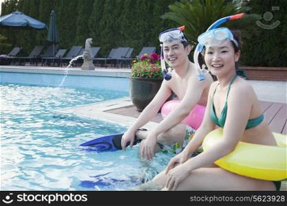 Portrait of smiling couple in snorkeling gear sitting by the edge of the pool and looking at camera