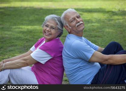 Portrait of smiling couple sitting back to back in a park