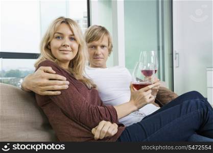 Portrait of smiling couple with wine glasses in living room at home
