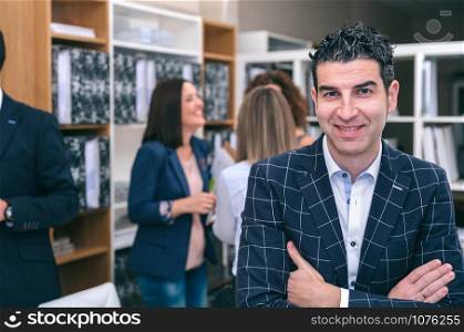 Portrait of smiling curly businessman looking at camera in the office with colleagues talking on background. Portrait of smiling businessman looking at camera in office