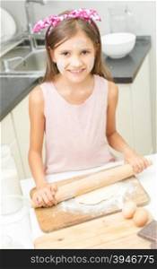 Portrait of smiling cute girl rolling dough with wooden pin on kitchen