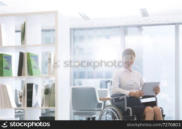Portrait of smiling disabled businesswoman with digital tablet sitting on wheelchair at office