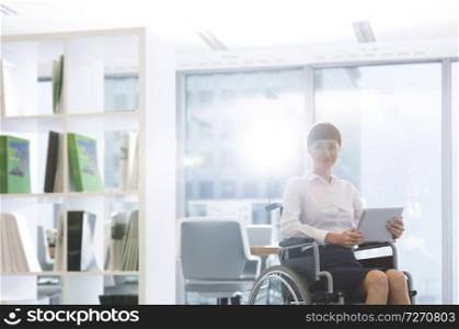 Portrait of smiling disabled businesswoman with digital tablet sitting on wheelchair at office