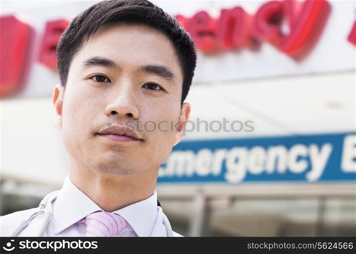Portrait of smiling doctor outside of the hospital, emergency room sign in the background, Close-Up