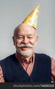 Portrait of smiling elderly man in party cap isolated on grey background. Cheerful mature senior looking at camera in studio. Portrait of smiling elderly man in cap