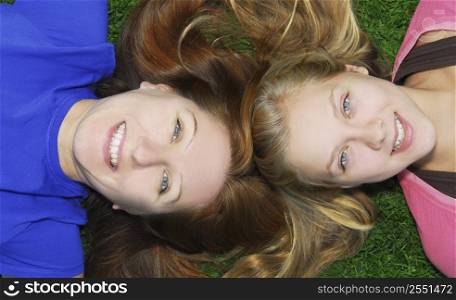 Portrait of smiling family of mother and her teenage daughter lying on grass in summer park