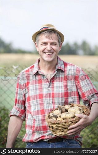 Portrait of smiling farmer carrying organic potatoes in basket at farm