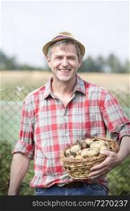 Portrait of smiling farmer carrying organic potatoes in basket at farm