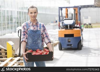 Portrait of smiling farmer with tomatoes in crate against forklift