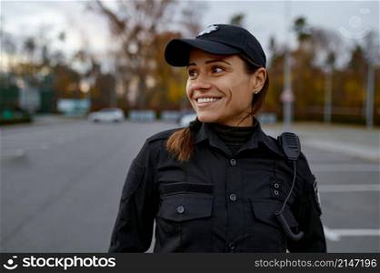 Portrait of smiling female police officer on street looking aside. Shot with blurred background. Portrait of smiling police woman on street