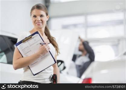 Portrait of smiling female repair worker with clipboard in car workshop