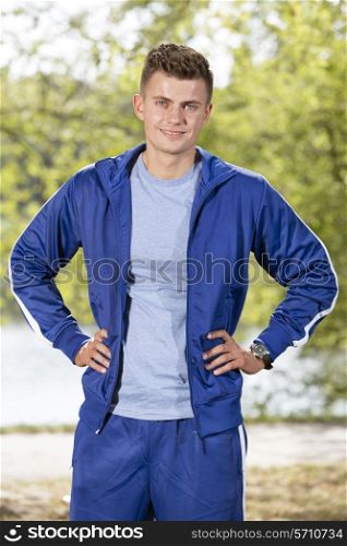 Portrait of smiling fit man standing with hands on hips in park