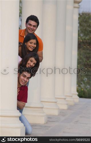 Portrait of smiling friends peeking from behind column outdoors