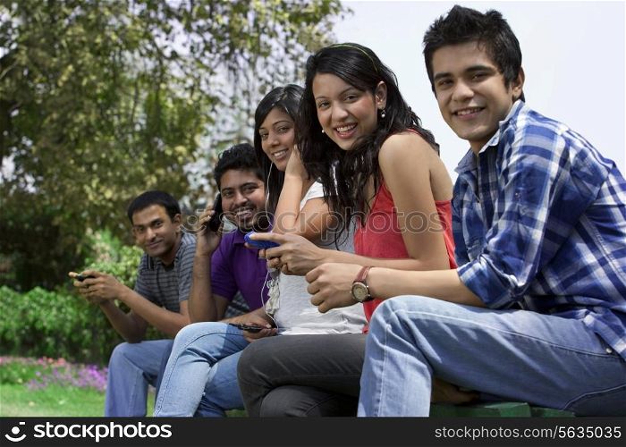 Portrait of smiling friends using cell phone in lawn