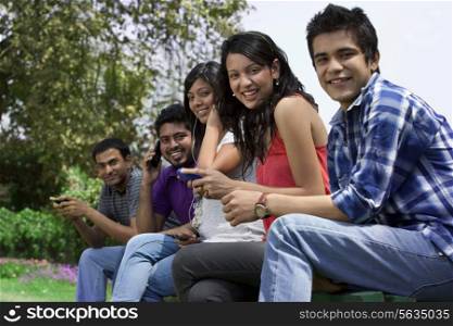 Portrait of smiling friends using cell phone in lawn