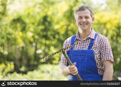 Portrait of smiling gardener holding rake in plant nursery