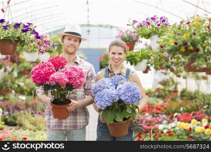 Portrait of smiling gardeners holding flower pots at greenhouse