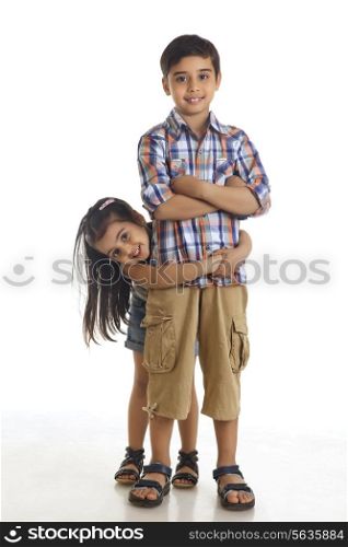 Portrait of smiling girl embracing brother from behind against white background