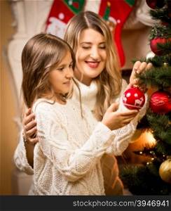 Portrait of smiling girl helping mother to decorate Christmas tree