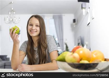 Portrait of smiling girl holding apple while sitting at table in house