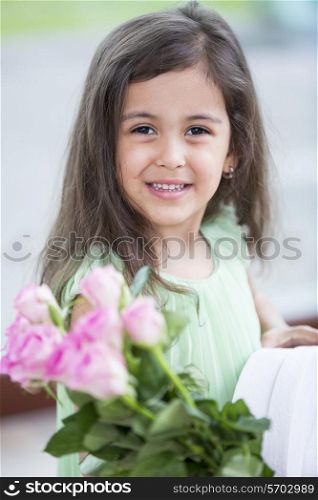 Portrait of smiling girl holding roses and gift box at home