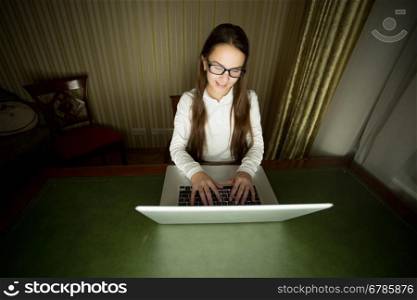 Portrait of smiling girl in eyeglasses using laptop at late evening