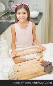 Portrait of smiling girl rolling dough with wooden pin on kitchen
