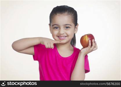 Portrait of smiling girl showing apple against colored background